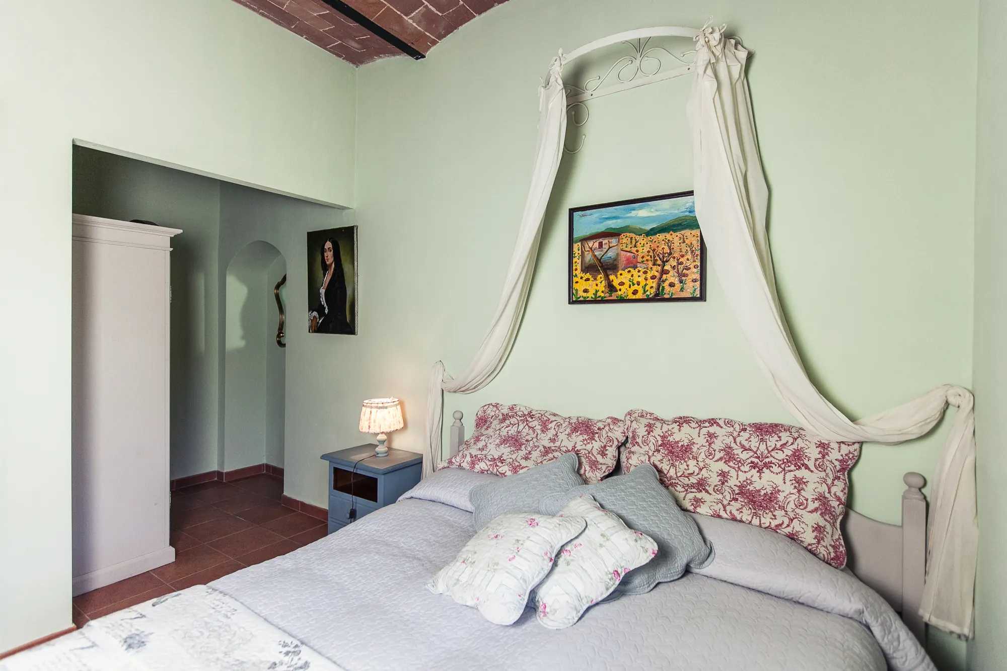 Camera da letto con letto matrimoniale, comodino con lampada e quadri alle pareti