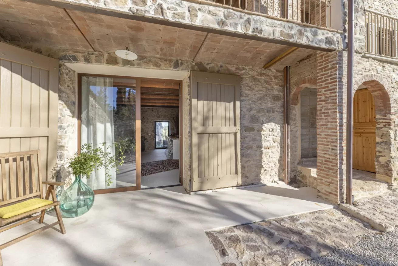 Portico in pietra con porta a vetri, persiane beige e una sedia con vaso decorativo