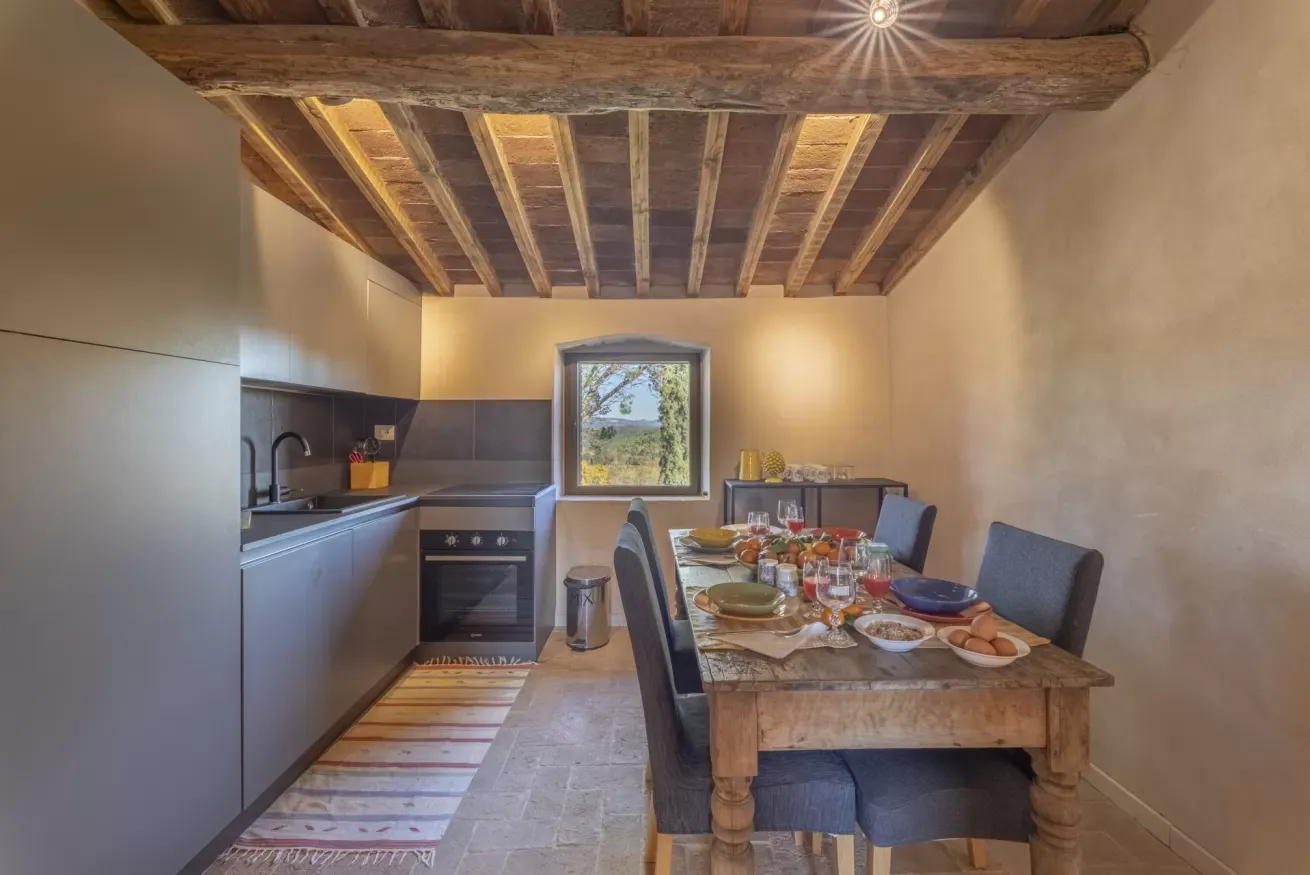 Cucina rustica con tavolo apparecchiato per un pasto, travi in legno a vista e finestra sul paesaggio esterno