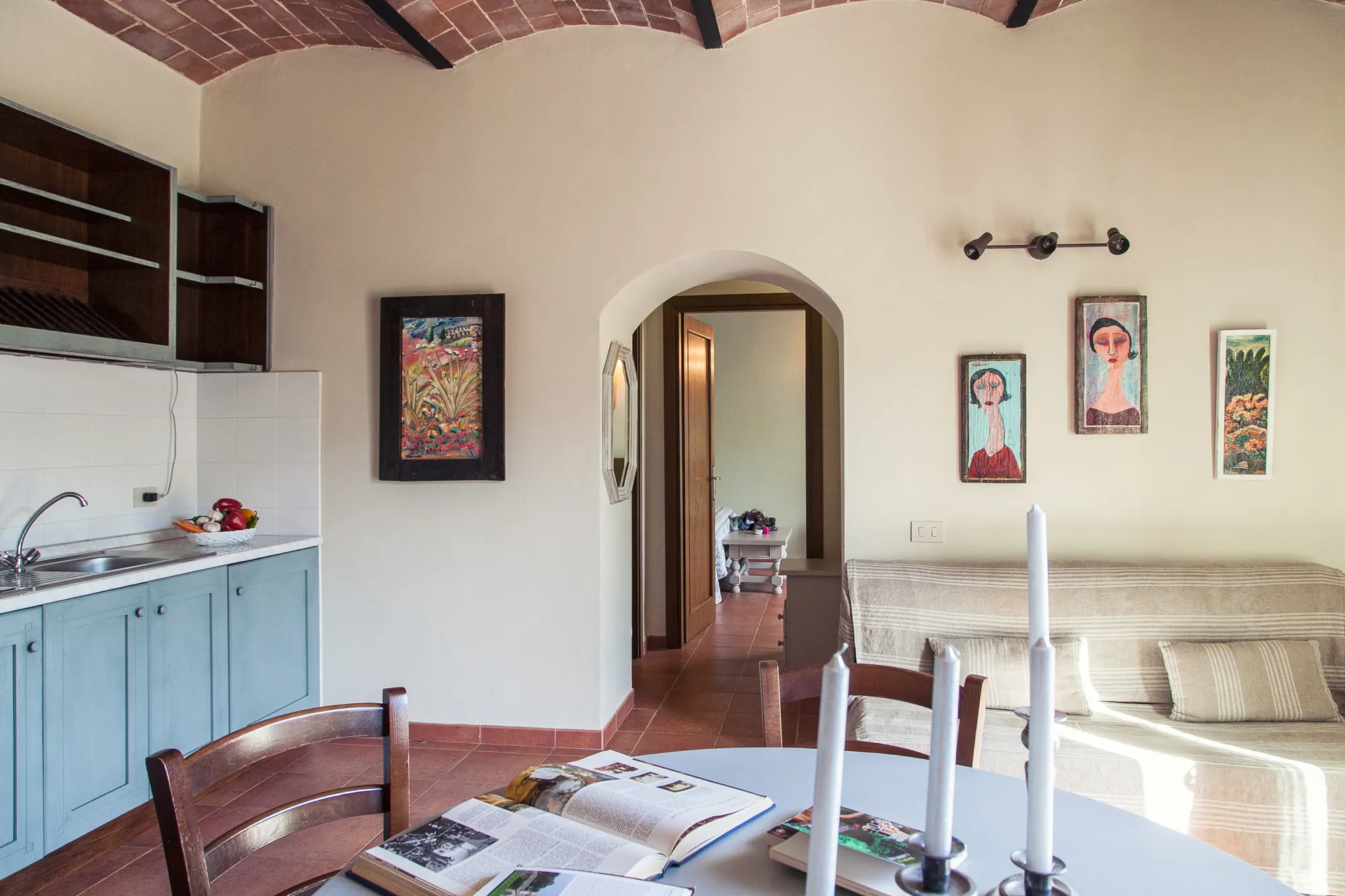 Interno di soggiorno con angolo cucina, divano, tavolo apparecchiato e quadri alle pareti