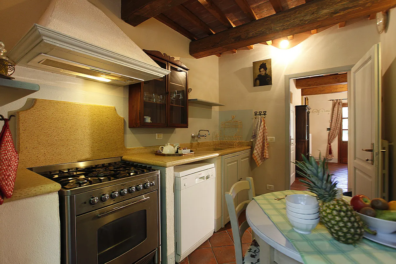 Cucina rustica con tavolo apparecchiato, forno, lavastoviglie e travi in legno a vista