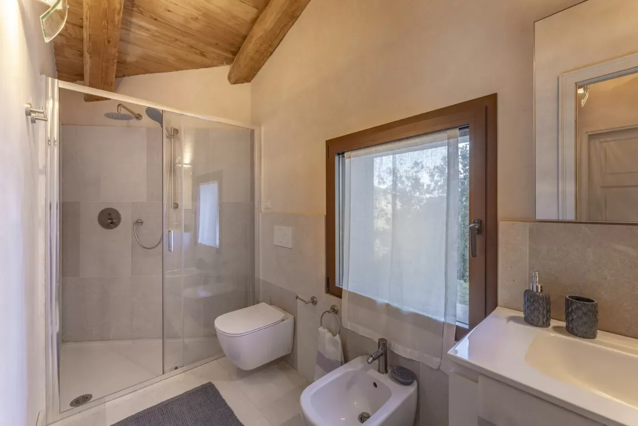 Bagno moderno con doccia in vetro, lavabo, bidet e finestra con tenda
