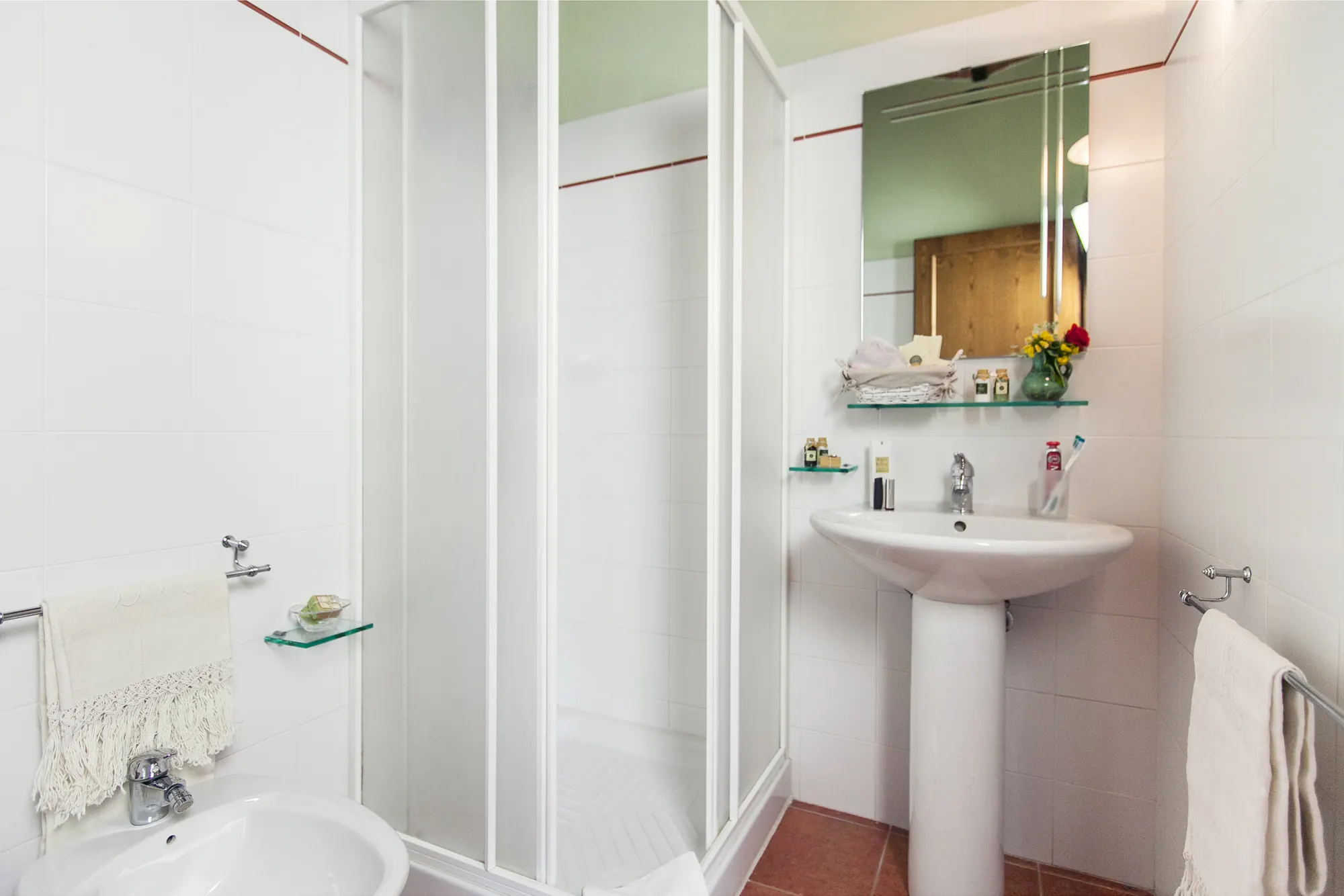 Bagno con doccia, lavabo e specchio, con asciugamani e ripiani in vetro