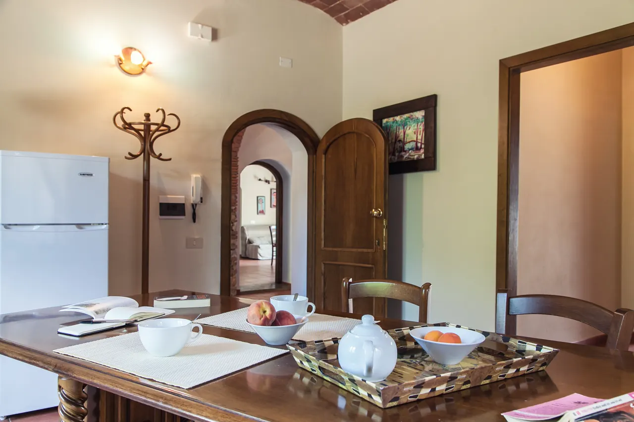 Sala da pranzo con tavolo apparecchiato, frutta e una teiera, in una casa con archi e porte in legno