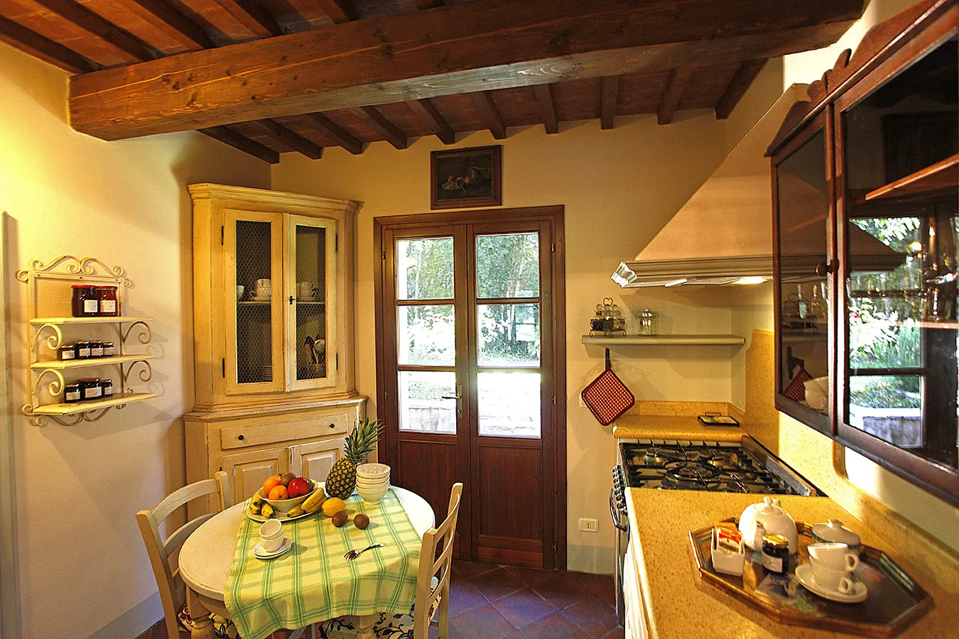 Cucina rustica con tavolo apparecchiato, credenza, piano cottura e finestre sul giardino