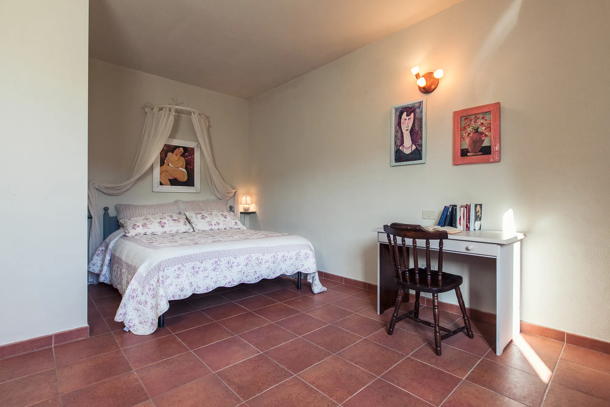 Camera da letto con letto matrimoniale, scrivania e sedia, quadri alle pareti e luce naturale