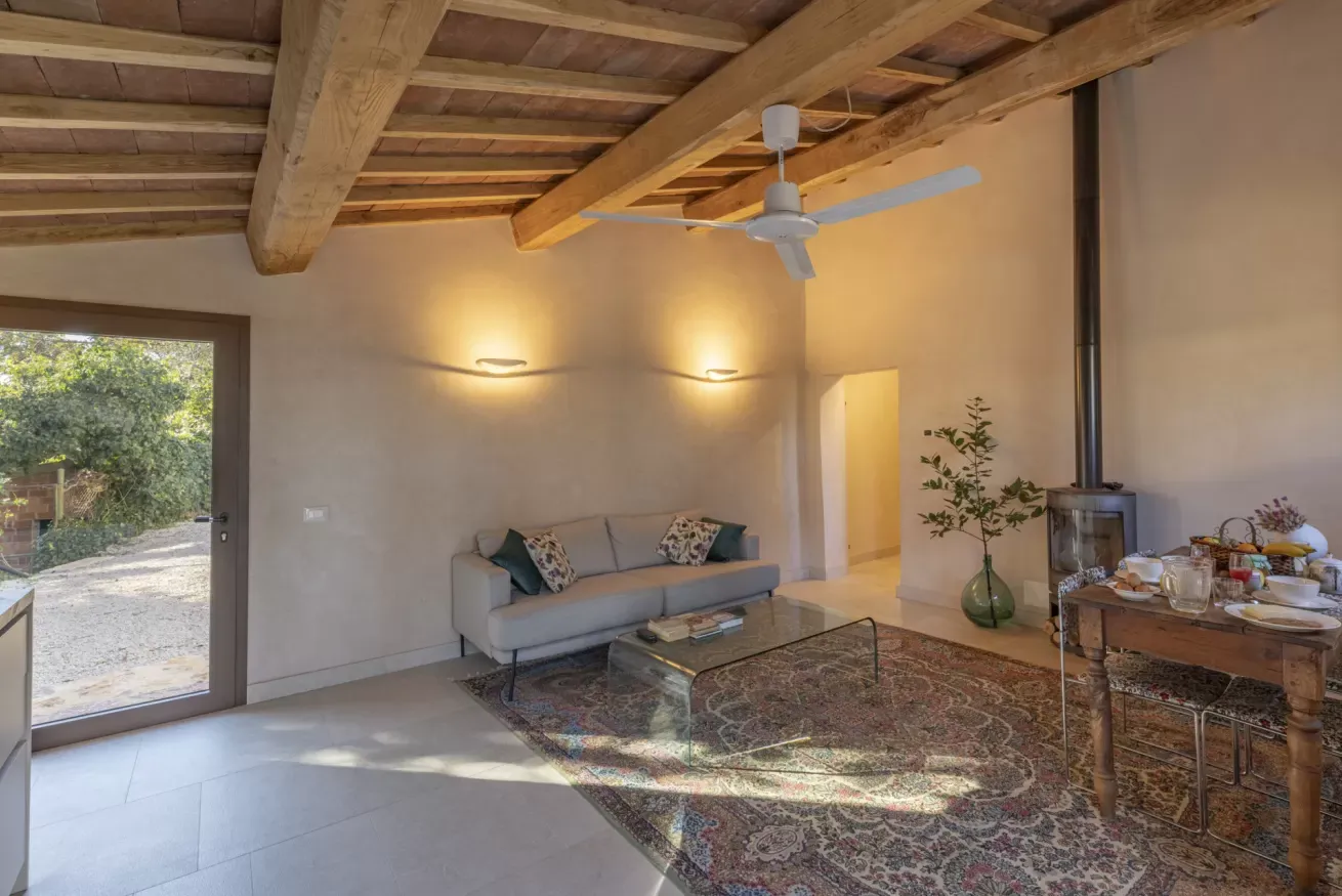 Soggiorno con soffitto in legno, camino, divano, tavolo apparecchiato e porta finestra sul giardino