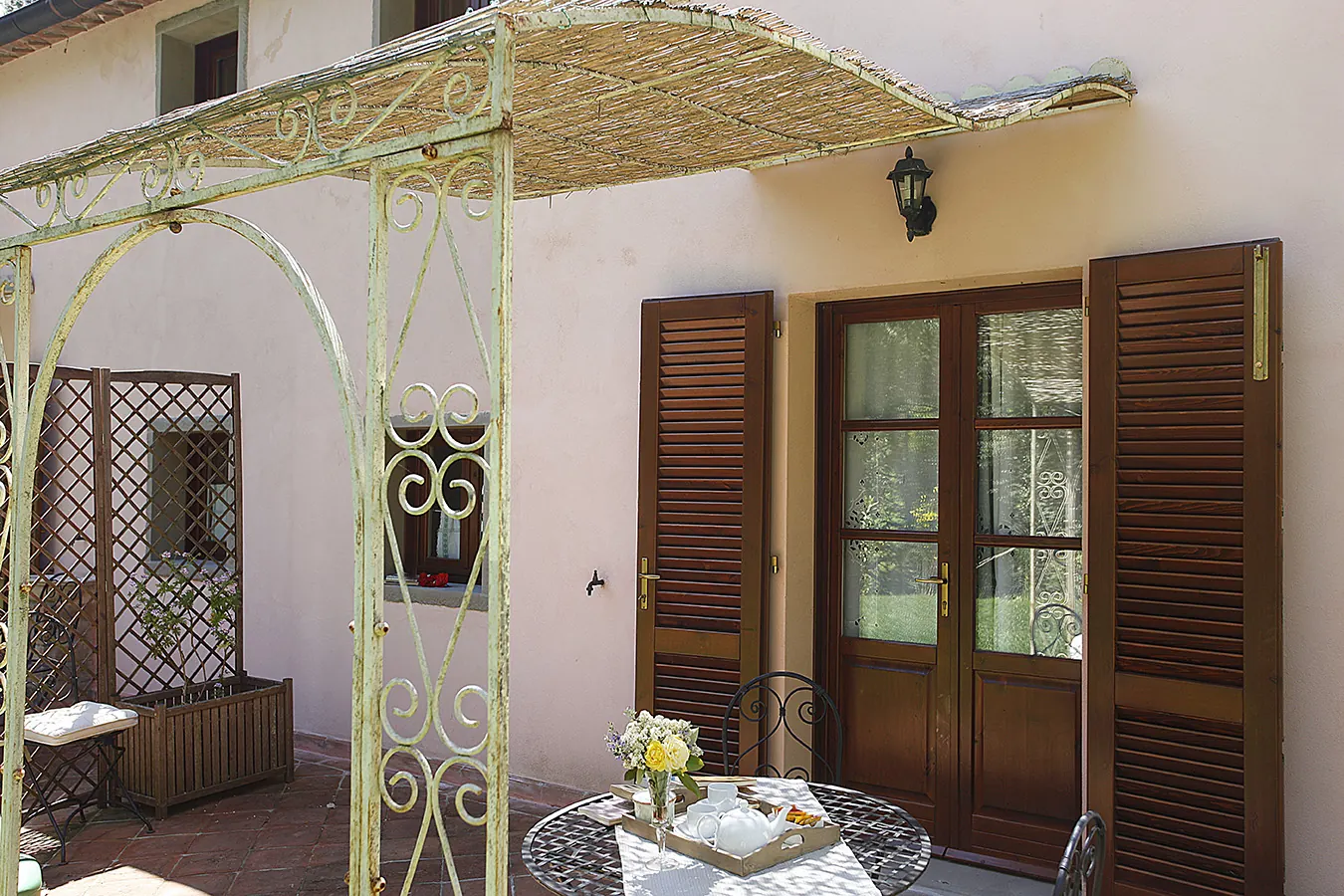 Patio con pergolato, tavolino apparecchiato e porte-finestre con persiane aperte