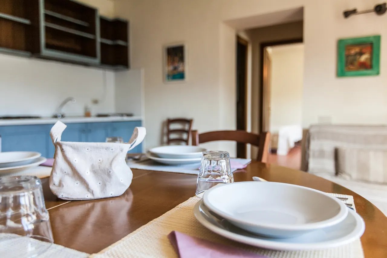 Tavolo apparecchiato in una cucina-soggiorno con piatti, bicchieri e una borsa di stoffa al centro