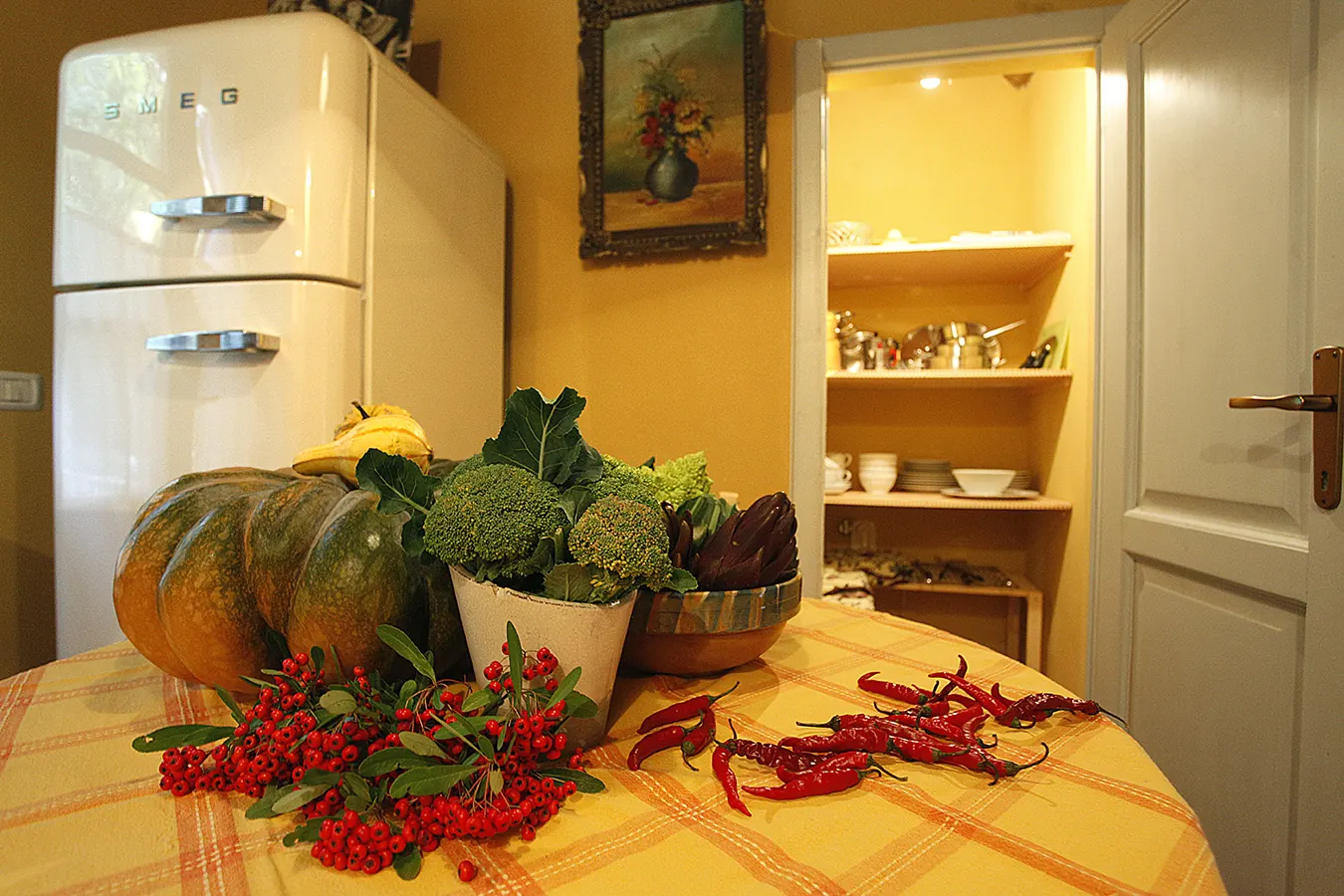 Tavolo in cucina con zucca, broccoli, peperoncini e bacche rosse davanti a un frigorifero aperto