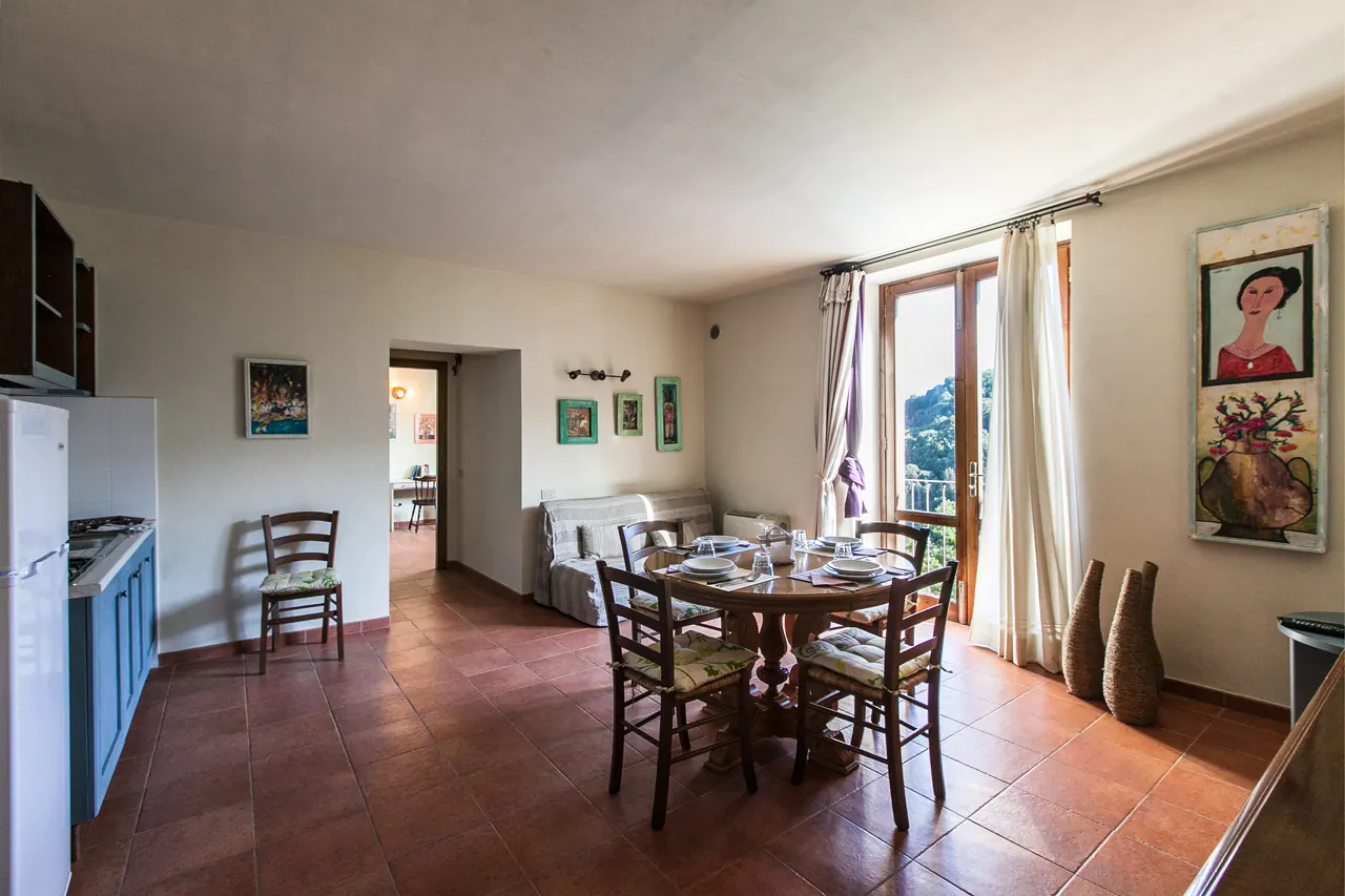 Soggiorno con tavolo da pranzo apparecchiato, cucina a vista e finestra aperta sul balcone