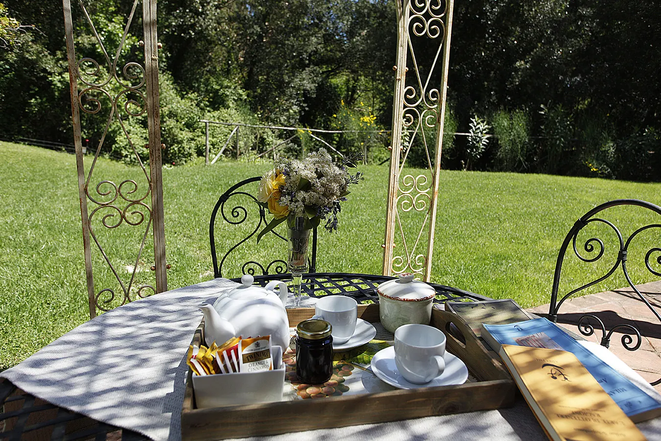 Tavolo da tè all’aperto in giardino con teiera, tazze, biscotti e un vaso di fiori