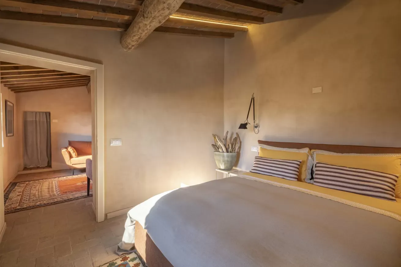 Camera da letto con letto matrimoniale, travi a vista e accesso a un salottino adiacente