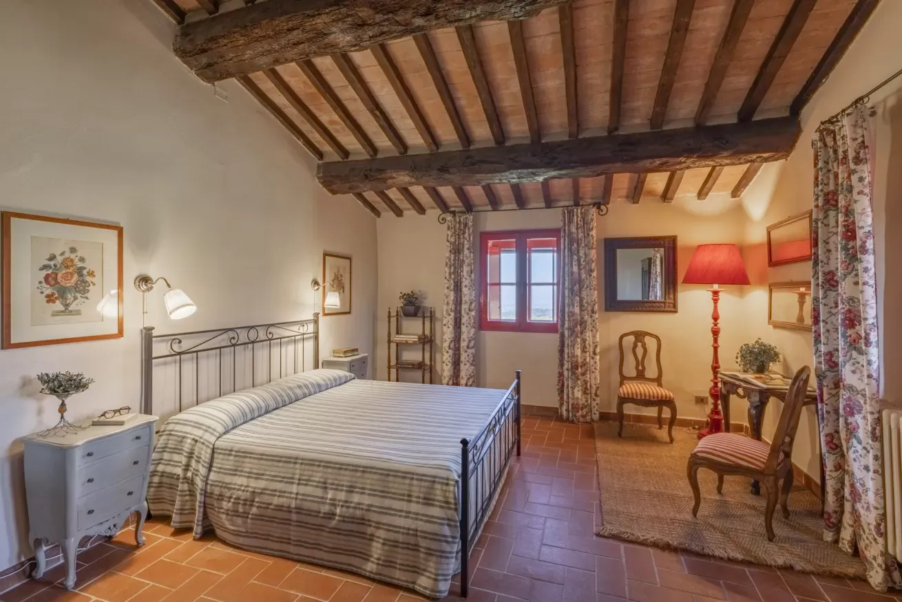 Rustic bedroom with exposed wooden beams, a metal bed, and a small sitting area