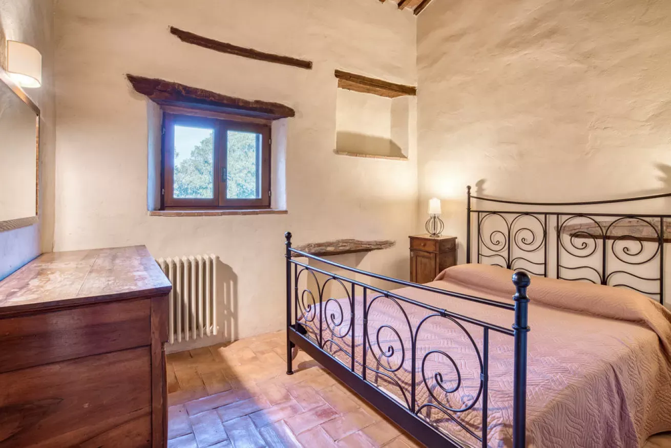 Rustic bedroom with wrought-iron bed, wooden dresser, and window