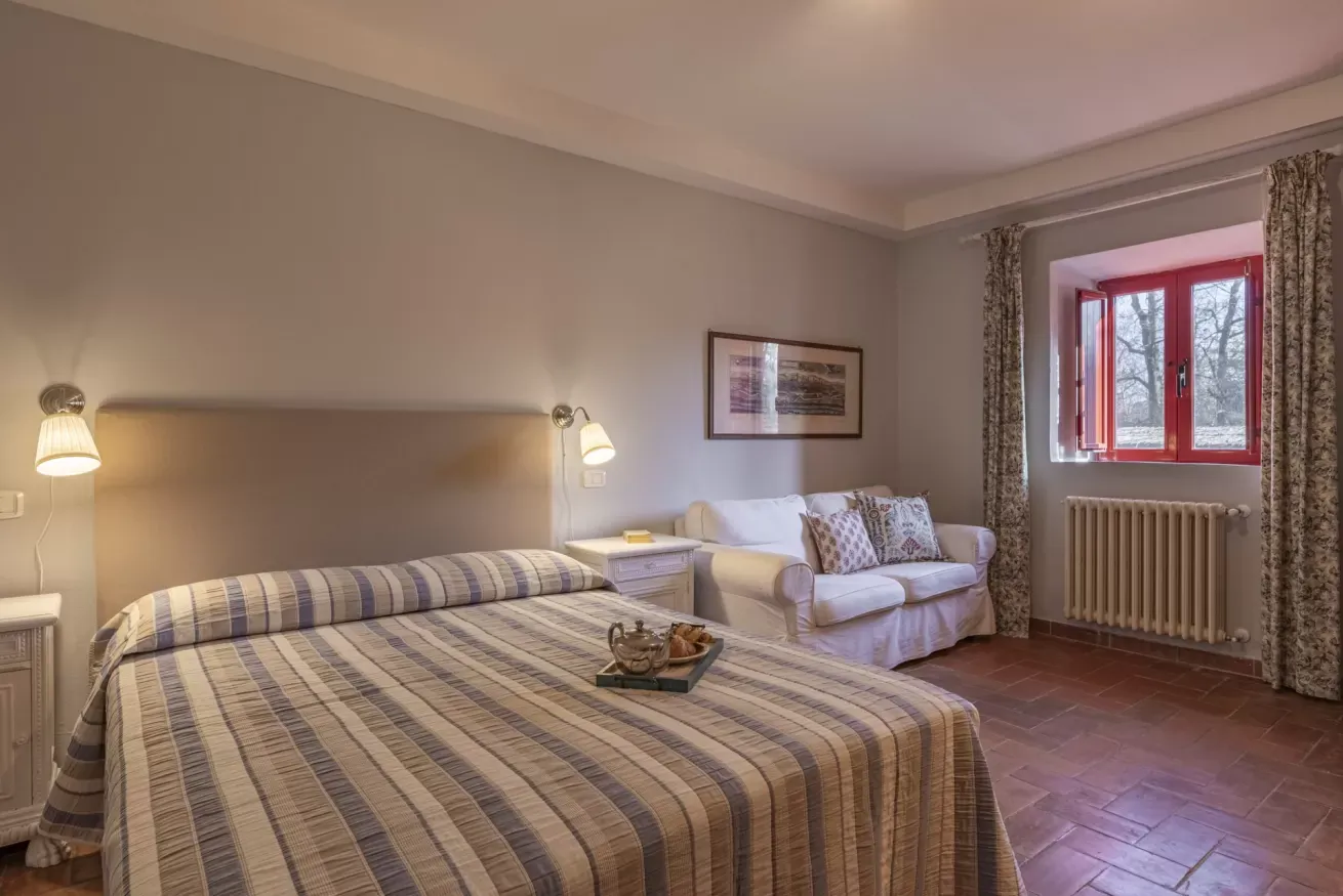 Bedroom with a striped bedspread, sofa, wall lamps, and a red-framed window