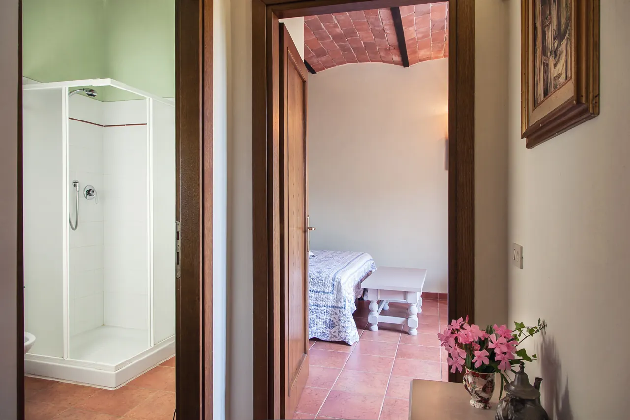 Corridoio con bagno a sinistra e camera da letto in fondo, con tavolino e fiori in primo piano