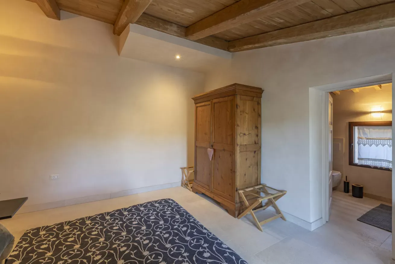 Camera da letto con soffitto in legno, armadio in legno e bagno visibile dalla porta aperta
