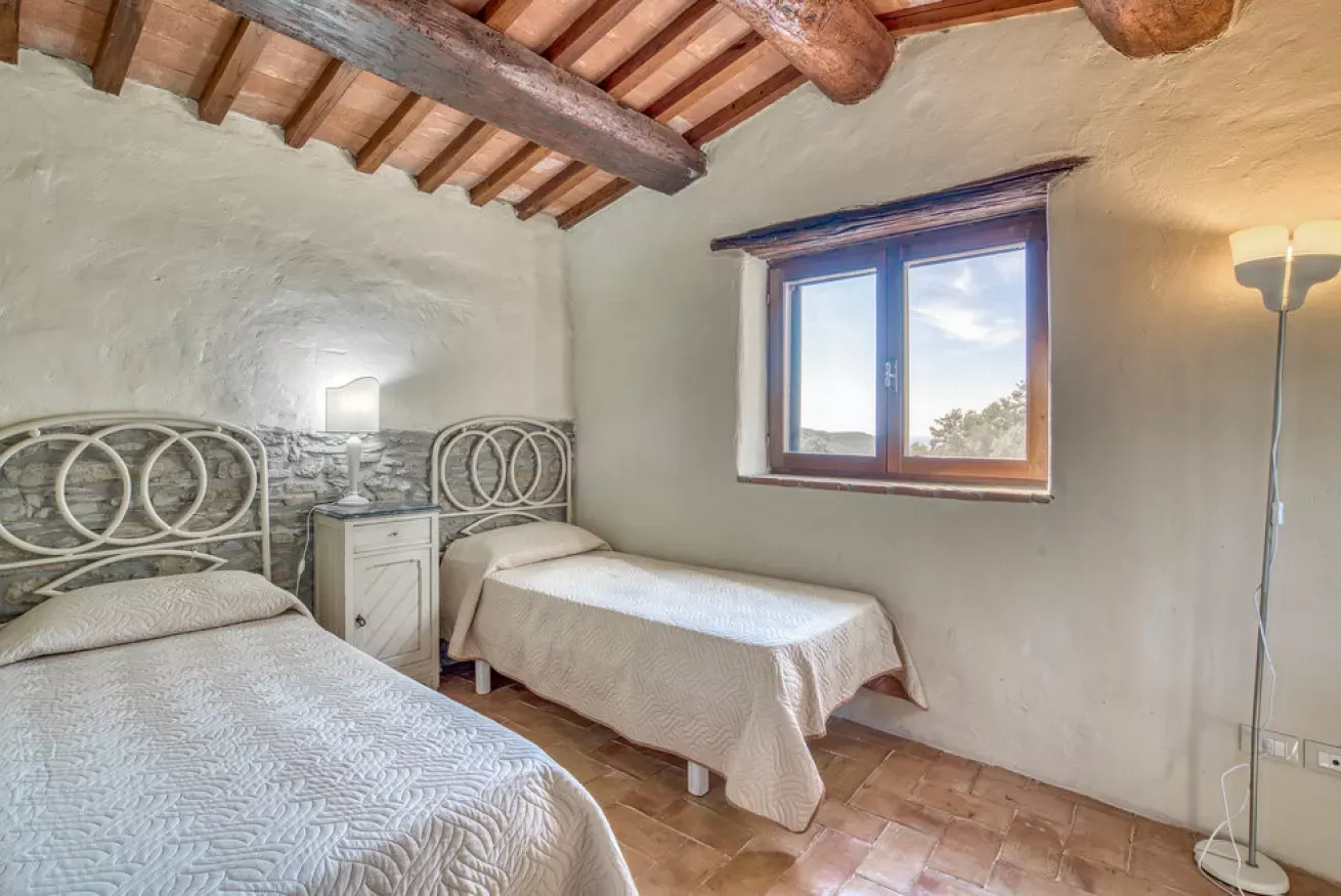 Rustic bedroom with two single beds, a window, and exposed wooden ceiling beams