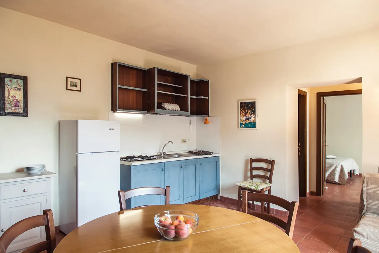 Cucina-soggiorno con tavolo rotondo, frigorifero, lavello e accesso alla camera da letto