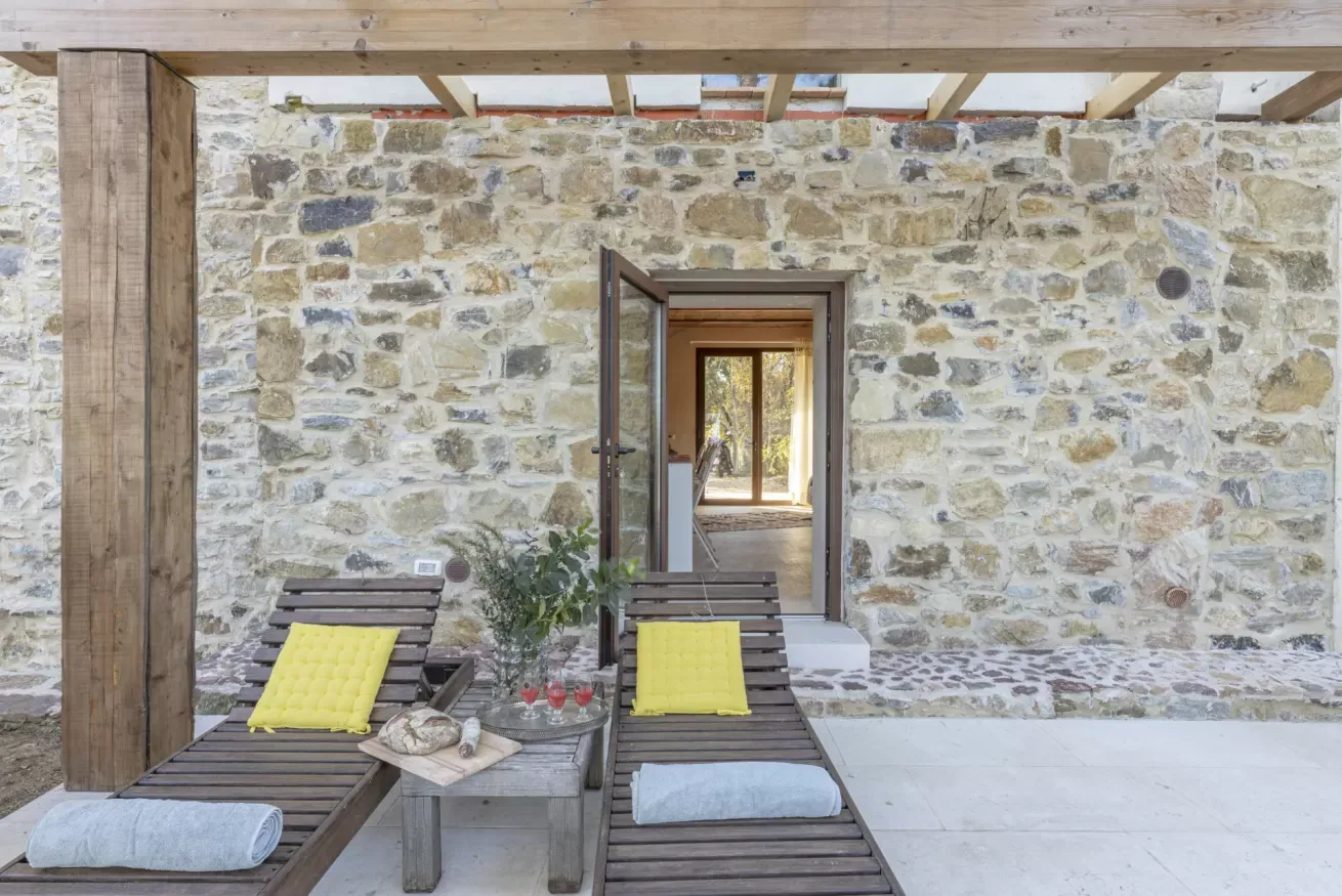 Terrazza con due lettini, tavolino e parete in pietra con porta aperta