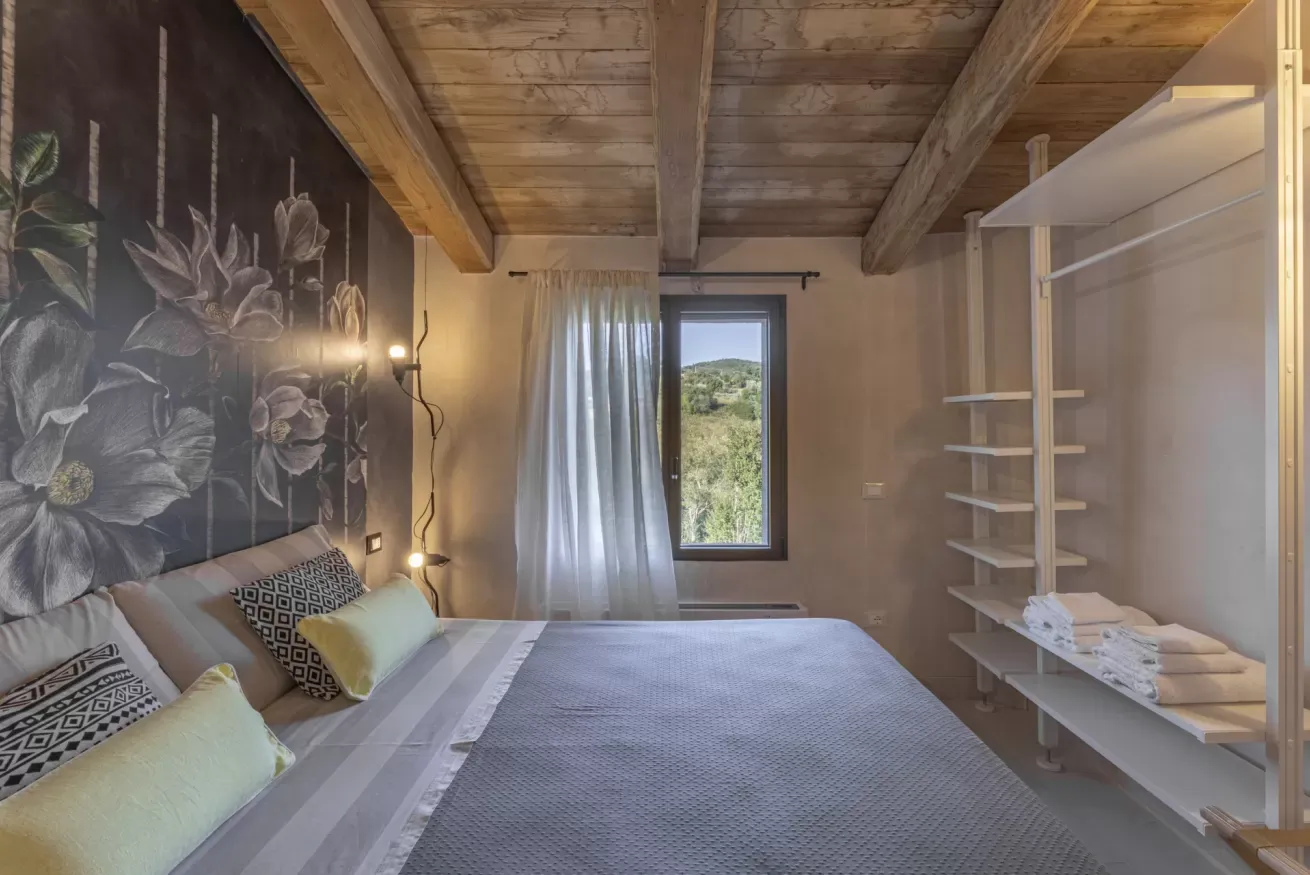 Camera da letto con letto matrimoniale, parete decorata con fiori e finestra con vista sul verde
