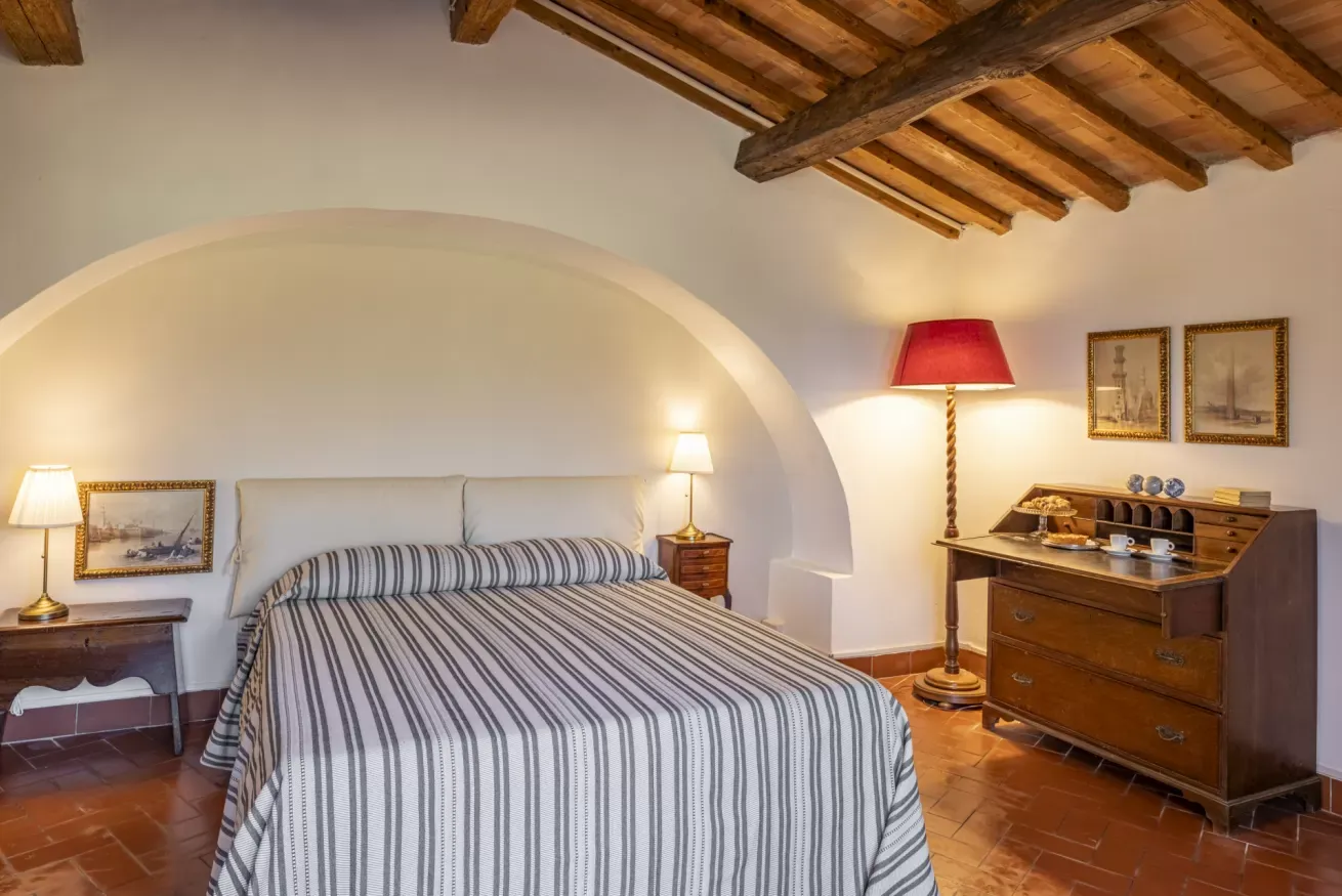 Rustic bedroom with a striped bedspread, wooden ceiling beams, and vintage lamps and furniture