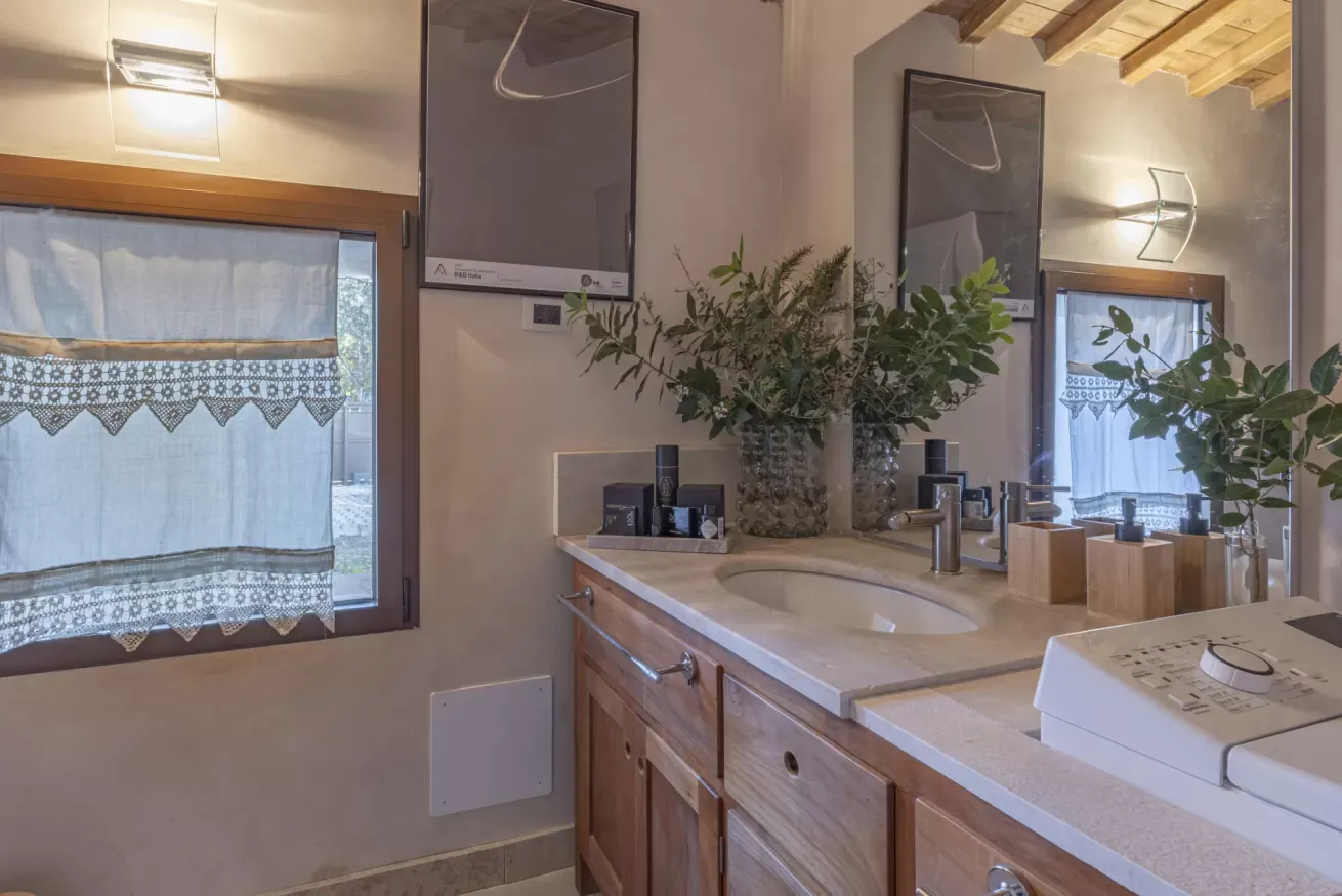 Bagno con lavabo in legno, specchio grande, finestre con tende e piante decorative