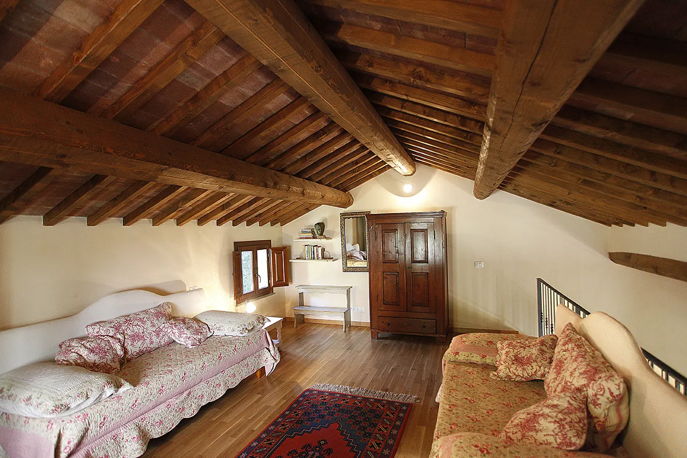Camera mansardata con travi in legno a vista, due divani letto, armadio e piccolo tappeto orientale
