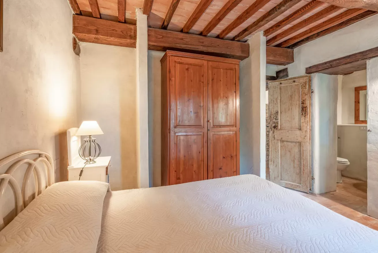 Bedroom with a white bed, bedside lamp, wooden wardrobe, and an open door to a bathroom