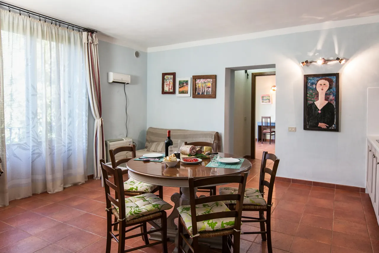 Sala da pranzo luminosa con tavolo apparecchiato, sedie in legno e quadri alle pareti
