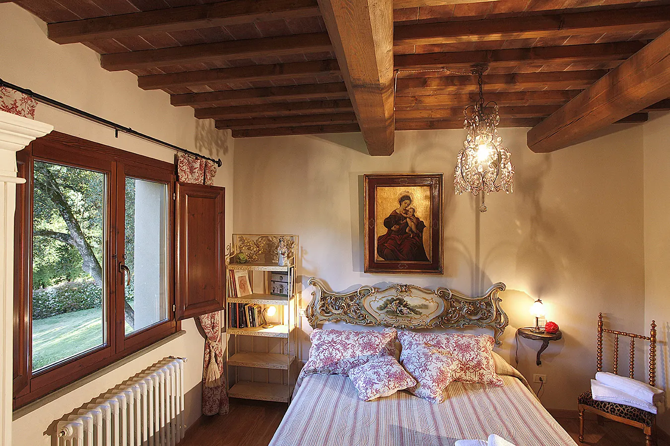 Camera da letto rustica con letto matrimoniale, travi in legno a vista, finestra aperta e lampadario decorativo