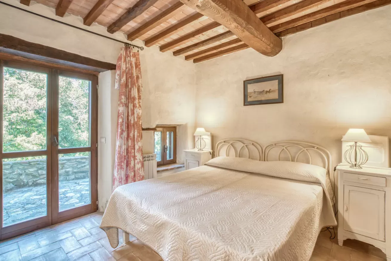 Cozy bedroom with a double bed, bedside lamps, exposed wooden beams, and French doors to a patio