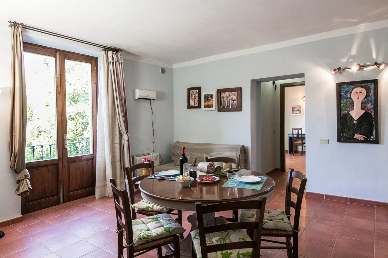 Sala da pranzo con tavolo apparecchiato, sedie, divano e porta finestra aperta sul verde