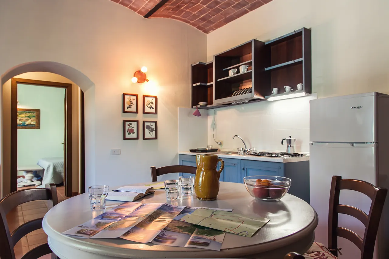 Cucina con tavolo apparecchiato, frigorifero, pensili e accesso a una stanza adiacente