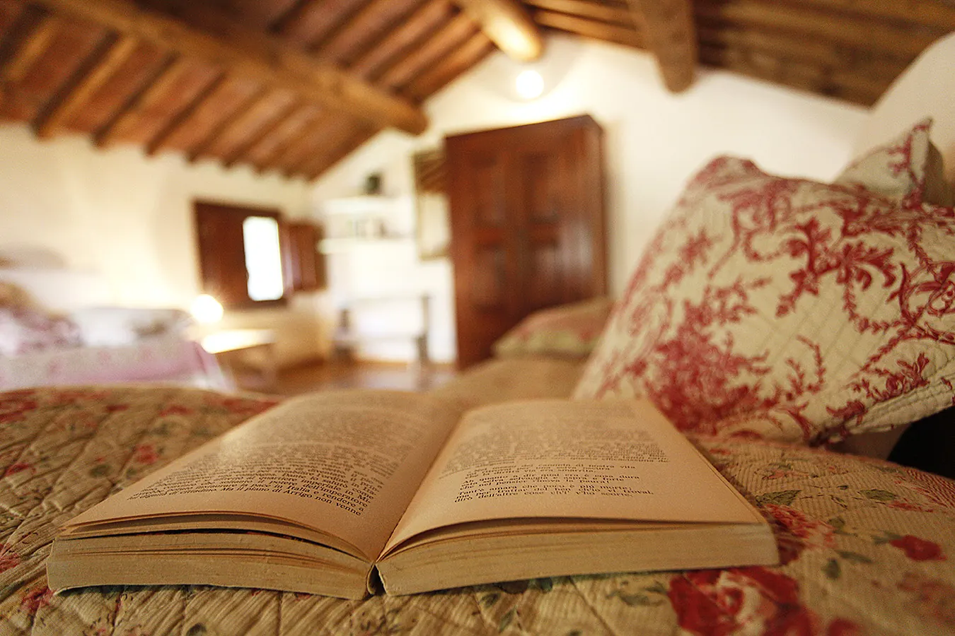 Libro aperto su un letto in una stanza accogliente con travi in legno e cuscini decorati