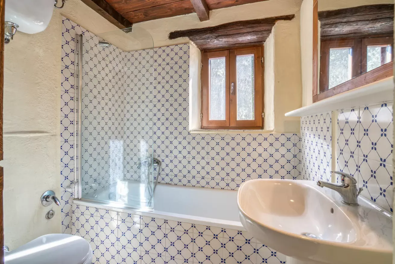 Bathroom with tiled tub, sink, and window under wooden beams