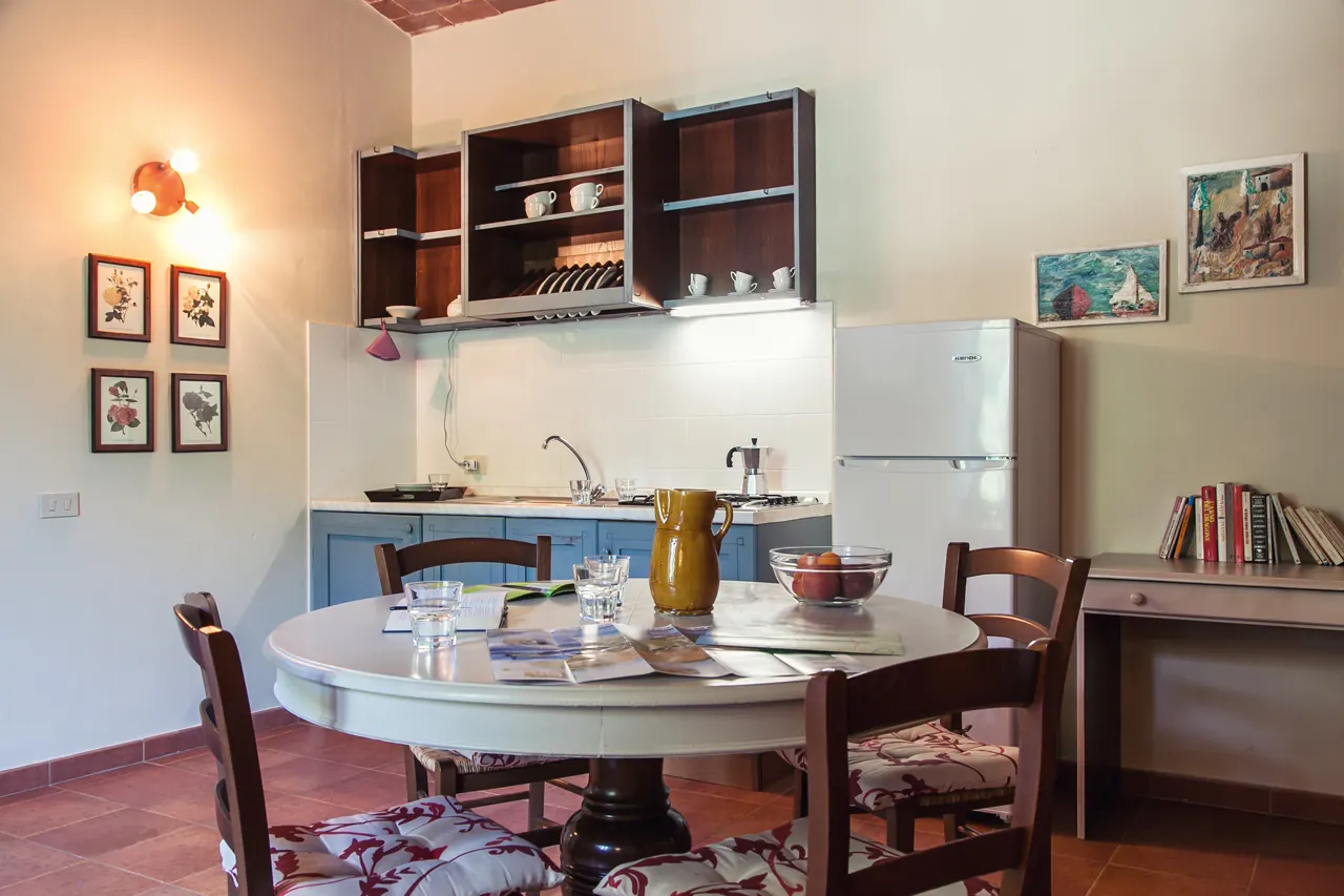 Cucina e zona pranzo con tavolo rotondo apparecchiato, mobili azzurri e frigorifero bianco