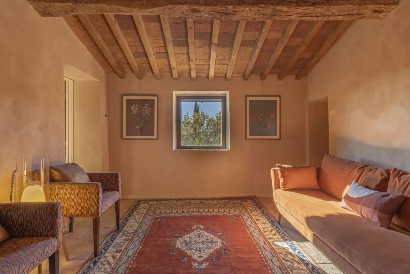 Salotto accogliente con soffitto in legno, divano, poltrone, tappeto e finestra centrale