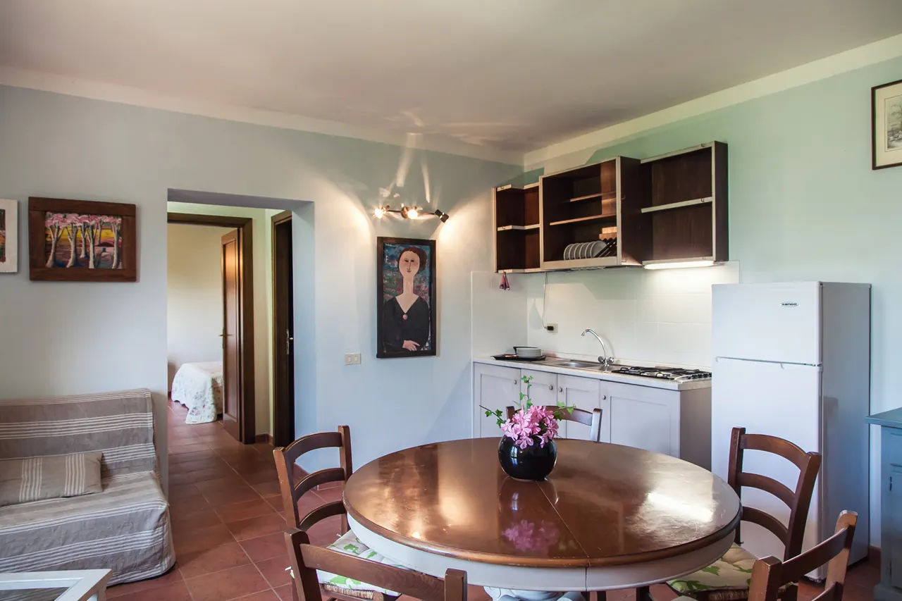 Cucina-soggiorno con tavolo rotondo, divano, frigorifero e pensili aperti