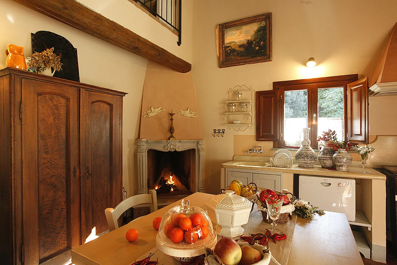 Cucina rustica con camino acceso, tavolo apparecchiato e finestra aperta sul giardino