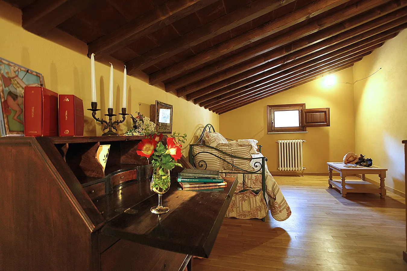 Camera da letto mansardata con letto in ferro battuto, pianoforte e tavolino accanto alla finestra