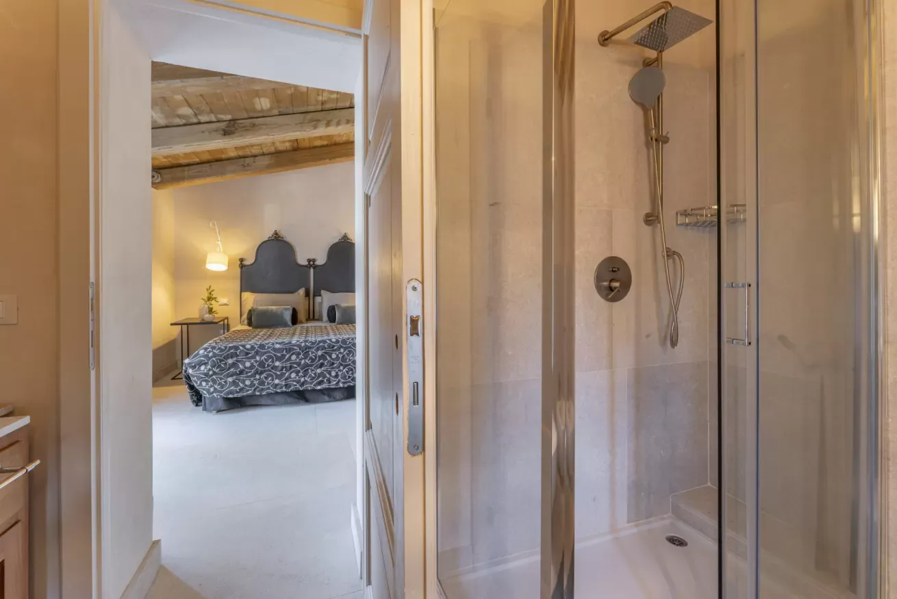 Bagno con doccia in primo piano e camera da letto visibile sullo sfondo