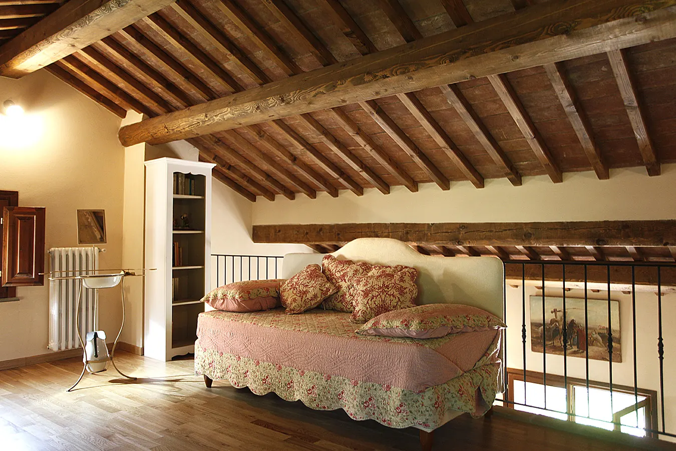 Camera da letto in mansarda con travi in legno a vista, letto imbottito e libreria bianca
