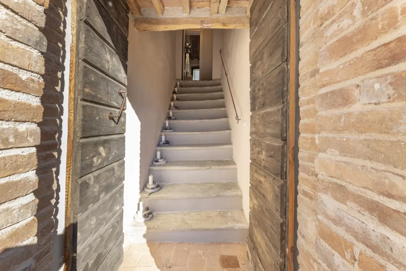 Scala in pietra vista attraverso una porta in legno, con candele sui gradini