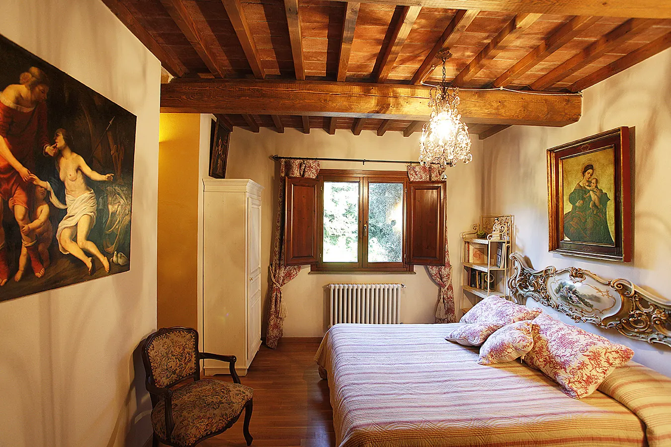 Camera da letto rustica con letto matrimoniale, travi a vista e dipinti alle pareti
