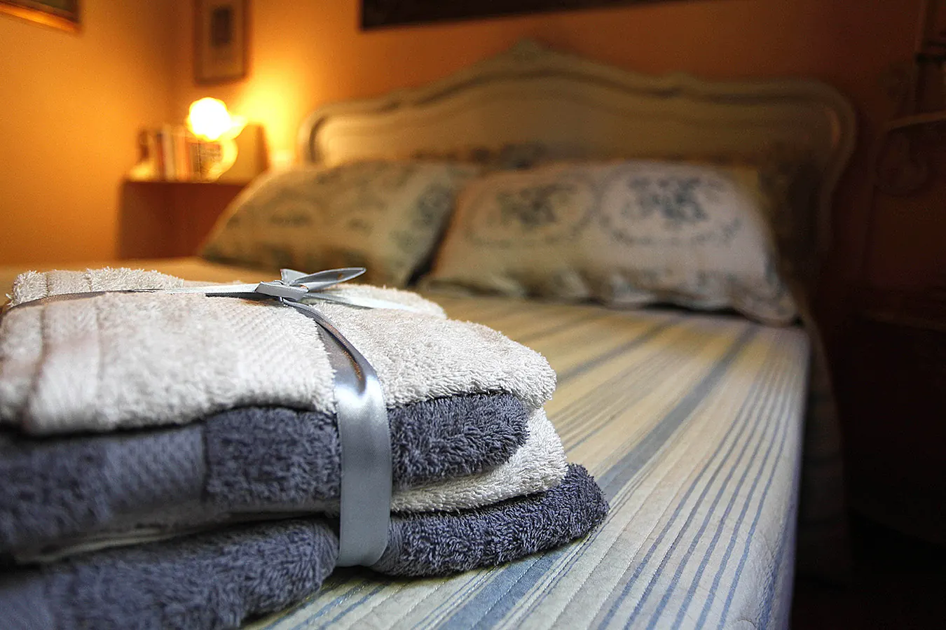 Asciugamani piegati con un nastro su un letto in una camera da letto illuminata da una lampada soffusa