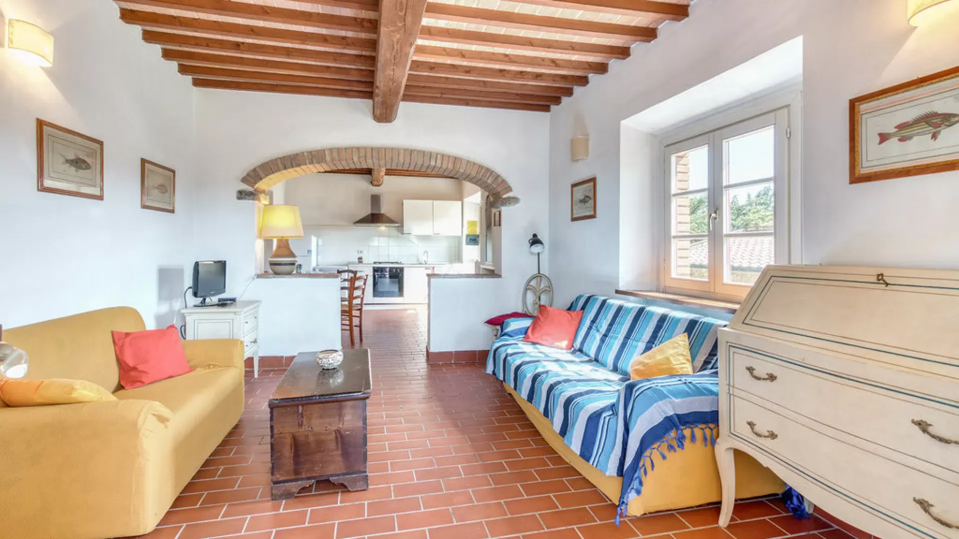 Bright living room with two sofas, exposed wood beams, and an open kitchen beyond the archway