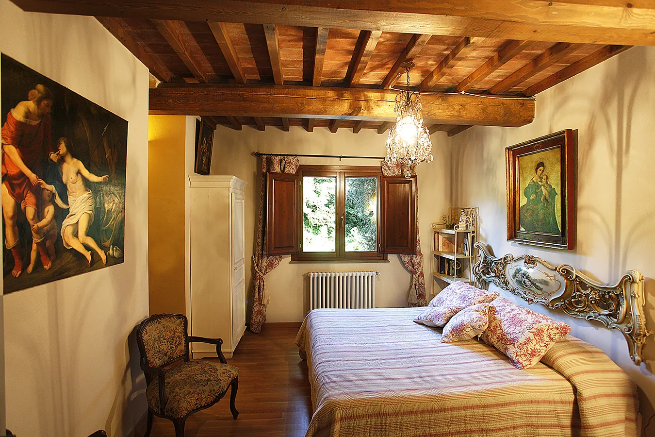 Camera da letto in stile classico con travi a vista, letto matrimoniale, finestra centrale e quadri alle pareti