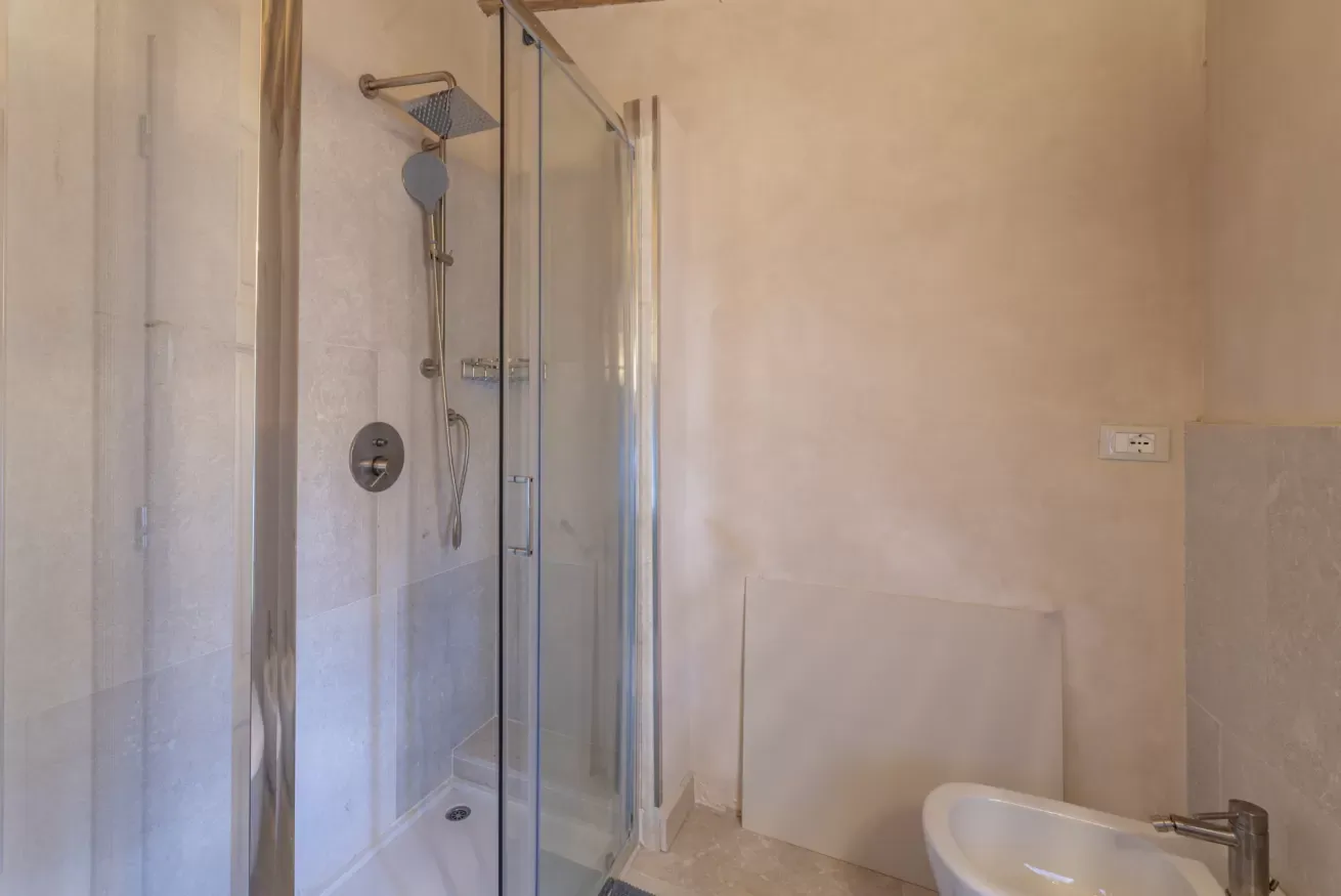 Bagno con cabina doccia in vetro e lavabo parzialmente visibile